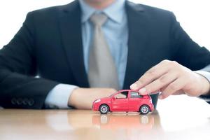 homme d'affaires près d'un bureau tenant une petite voiture. photo