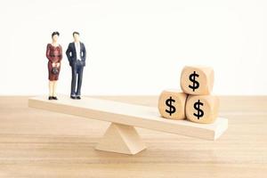 concept d'équilibre vie-travail ou argent. figurine de couple et symbole du dollar sur des blocs de bois sur une balançoire en bois photo