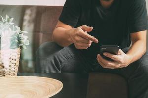 main d'homme designer utilisant un téléphone intelligent pour les achats en ligne de paiements mobiles, canal omni, assis sur un canapé dans le salon, vase en rotin avec plante et plateau en bois sur table, filtre photo