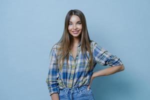 charmante jolie dame du millénaire garde la main sur la silhouette, se tient confiante et sourit joyeusement, porte une chemise à carreaux et un jean se tient dans une posture décontractée heureuse de rencontrer un ami aime parler agréablement photo