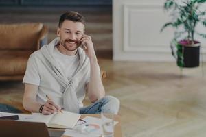 homme d'affaires heureux parlant au téléphone tout en étant assis à son bureau au bureau à domicile photo