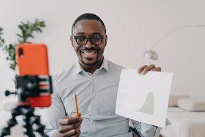 afro freelancer a un remue-méninges en ligne. un homme positif montre un tableau de données s'exprimant lors d'une conférence en ligne. photo