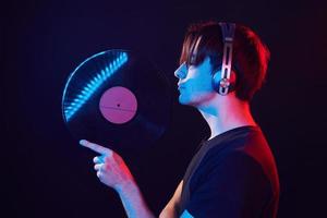 avec disque vinyle dans les mains. homme debout dans le studio avec néon photo