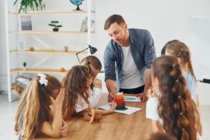 regardant le petit modèle de volcan. groupe d'enfants élèves en classe à l'école avec professeur photo