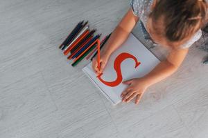 vue de dessus d'une petite fille qui écrit une lettre lorsqu'elle est allongée sur le sol à la maison photo