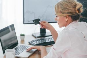 en utilisant la carte de crédit pour le paiement. femme courtier en valeurs mobilières en tenue de soirée travaille au bureau photo