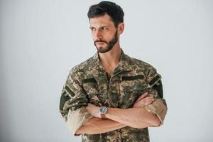 les bras croisés. soldat en uniforme se tient à l'intérieur contre un mur blanc photo