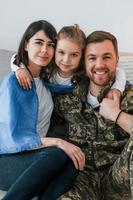 le drapeau ukrainien est sur les épaules. soldat en uniforme est à la maison avec sa femme et sa fille photo