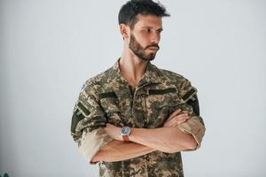 les bras croisés. soldat en uniforme se tient à l'intérieur contre un mur blanc photo