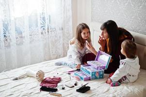 mère et filles se maquillant sur le lit dans la chambre. photo