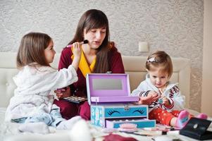 mère et filles se maquillant sur le lit dans la chambre. photo