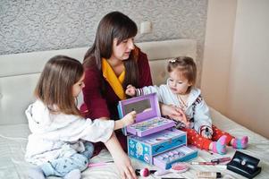 mère et filles se maquillant sur le lit dans la chambre. photo