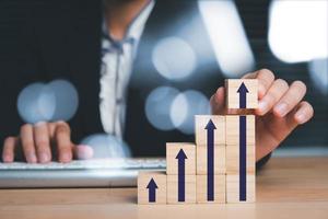 main de femme d'affaires tenant des cubes de blocs de bois empilés comme escalier avec flèche vers le haut sur le bureau, processus de réussite de la croissance du concept d'entreprise. photo