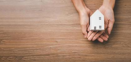 main de femme tenant une maison en bois sur fond jaune, logement pour sans-abri et concept d'assurance de protection de la maison, journée internationale des familles, enseignement à domicile, vue de dessus. photo