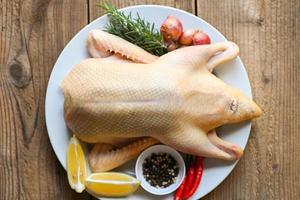 canard cru aux épices prêtes à cuire sur fond de bois , viande de canard fraîche sur assiette pour la nourriture , canard entier et citron romarin piment ail - vue de dessus photo