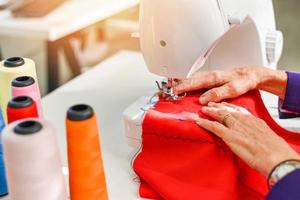 Senior woman tailleur travaillant à l'usine de couture - couturière faisant la machine à coudre coudre du tissu dans la salle d'exposition de vêtements de mode photo