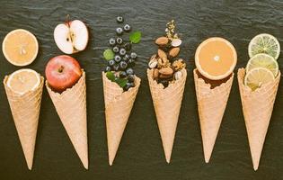 divers ingrédients pour la saveur de la crème glacée dans des cônes installés sur fond de pierre sombre.