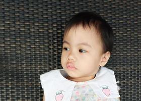 portrait d'une charmante petite fille asiatique de 3 ans assise sur une chaise marron foncé. photo