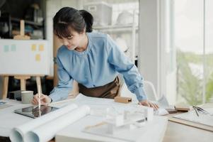 mise au point sélective, architecte ou ingénieure asiatique dessinant la conception de l'intérieur du bâtiment à l'aide d'une tablette. une femme architecte ou ingénieure asiatique s'assoit et analyse, conçoit des projets au bureau. photo