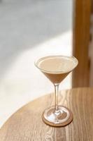 Cocktail de café au lait frais et élégant dans un verre à martini sur la table en bois sur la fenêtre latérale avec la lumière naturelle du soleil au café. photo