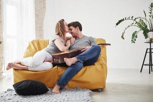 petite amie reconnaissante donne un baiser. couple heureux se reposant sur le canapé jaune dans le salon de leur nouvelle maison photo