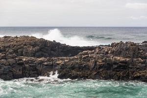 les vagues océaniques turbulentes avec de la mousse blanche battent les pierres côtières photo