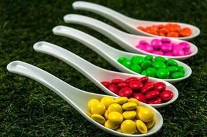 bonbons au chocolat colorés servis sur des cuillères avec fond d'herbe verte photo