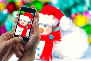 homme utilisant un téléphone portable pour regarder l'image agrandie du bonhomme de neige avec un arrière-plan flou. célébrer noël bonne année festival photo