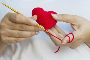 les mains de la dame faisant du crochet en forme de coeur rouge photo