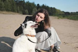 chien laika heureux souriant et assis à côté de son propriétaire. belle jeune femme caressant son chien assis sur une plage de sable. concept de convivialité et d'amour des animaux de compagnie photo