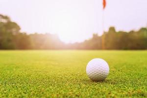 balle de golf sur l'herbe verte avec le lever du soleil photo