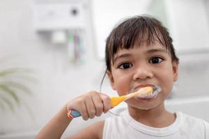 petite fille mignonne se nettoyant les dents avec une brosse à dents dans la salle de bain photo