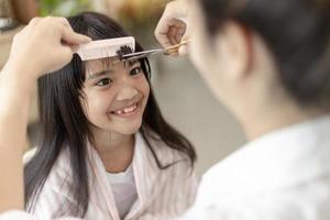 mère asiatique coupant les cheveux à sa fille dans le salon à la maison tout en restant à la maison à l'abri du coronavirus covid-19 pendant le verrouillage. concept d'auto-quarantaine et de distanciation sociale. photo