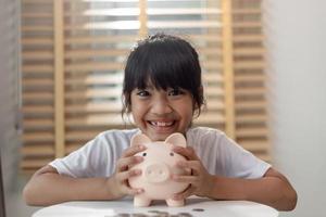 petite fille asiatique économisant de l'argent dans une tirelire, apprenant à économiser, enfant économisant de l'argent pour l'éducation future. concept d'argent, de finances, d'assurance et de personnes photo