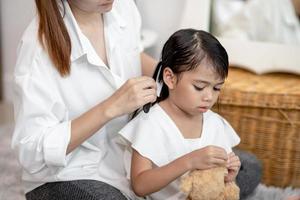 jeune mère asiatique attachant les cheveux de sa fille photo