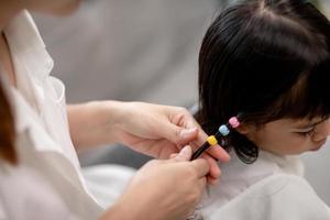 jeune mère asiatique attachant les cheveux de sa fille photo