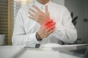 employé de sexe masculin assis au bureau avec un ordinateur portable, massant le poignet endolori, souffrant d'un nerf pincé, de muscles raides, du syndrome du canal carpien après avoir tapé sur un ordinateur portable photo