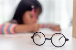 enfant asiatique étudiant retour à l'école ou enfant fille sourire écrire une note ou dessiner au crayon et lire sur une tablette d'ordinateur en faisant ses devoirs à une nouvelle idée penser ou les gens apprennent de la maison photo