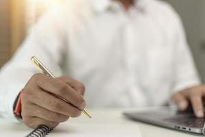 homme écrivant faisant la liste prenant des notes dans le bloc-notes travaillant ou apprenant sur un ordinateur portable à l'intérieur - cours éducatif ou formation, séminaire, concept d'éducation en ligne photo