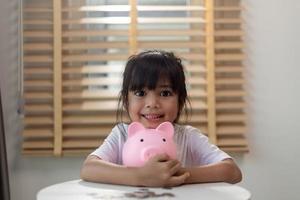 petite fille asiatique économisant de l'argent dans une tirelire, apprenant à économiser, enfant économisant de l'argent pour l'éducation future. concept d'argent, de finances, d'assurance et de personnes photo