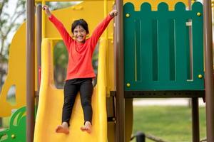 enfant jouant sur une aire de jeux extérieure. les enfants jouent dans la cour de l'école ou de la maternelle. enfant actif sur un toboggan et une balançoire colorés. activité estivale saine pour les enfants. petite fille escalade à l'extérieur. photo