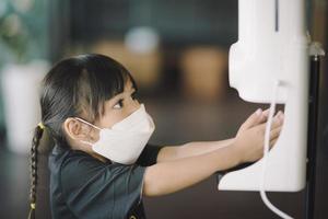 coronavirus covid-19 concept.petite fille chinoise asiatique portant un masque pour protéger le coronavirus et nettoyer les mains avec une pompe automatique de gel désinfectant à l'alcool avant de venir au restaurant pour arrêter le coronavirus.hygiène. photo