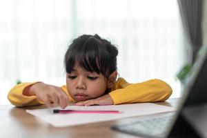 petite fille asiatique assise seule et regardant dehors avec un visage ennuyé, enfant d'âge préscolaire allongé sur la table avec triste ennuyé par les devoirs, enfant gâté photo