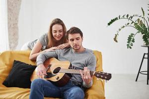 prendre un accord. jouer de la guitare acoustique pour la petite amie dans le salon de la nouvelle maison photo