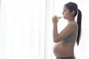 jeune femme enceinte buvant du lait à la maison, soins de santé et soins de grossesse photo