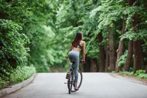 bois magnifiques. cycliste féminine sur un vélo sur route goudronnée dans la forêt pendant la journée photo