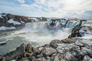 touriste européen assis au bord de la falaise devant godafoss la cascade de dieu l'un des lieux d'attraction touristique de la région nord de l'islande. photo