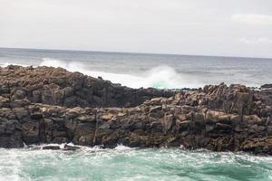 les vagues océaniques turbulentes avec de la mousse blanche battent les pierres côtières photo