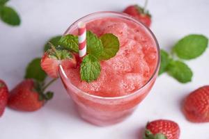 boire des smoothies fraise d'été, délicieux smoothie aux fraises garni de fraises fraîches et de menthe en verre. mise au point douce. belle apéritif fraise rose, concept de bien-être et de perte de poids photo