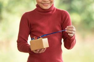 portrait de noël d'une petite fille souriante heureuse avec une boîte-cadeau près d'un arbre de branche verte. feuilles vertes bokeh hors focus arrière-plan de la forêt naturelle. photo